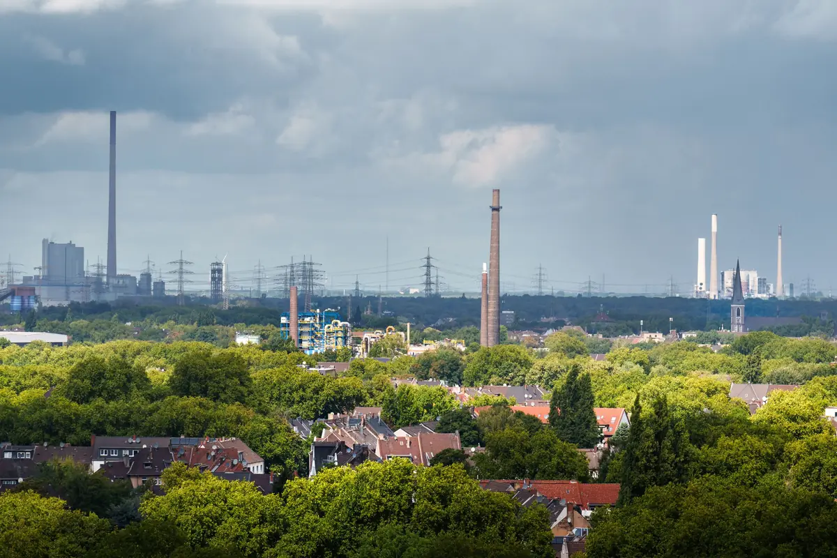 Wohnviertel zwischen Bäumen, dahinter Schornsteine und Kraftwerke – typisches Stadtbild im Ruhrgebiet