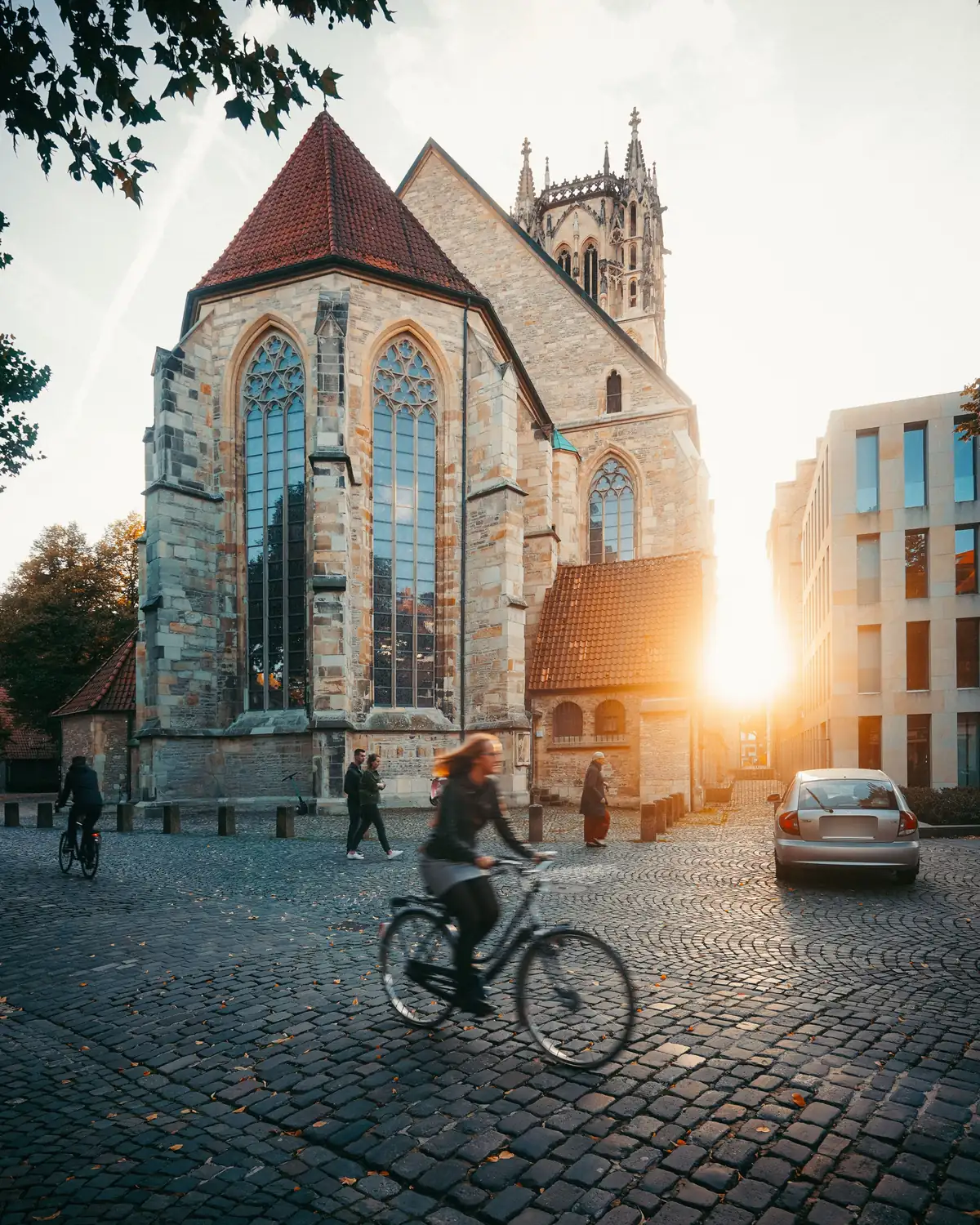 Gotische Kirche und Kopfsteinpflaster in der Altstadt von Münster, Radfahrerin im Vordergrund